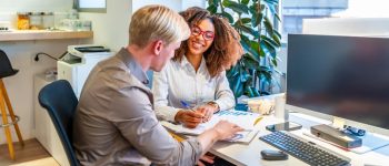 Two business colleagues are working together on a project, analyzing graphs and discussing strategies in a modern coworking office